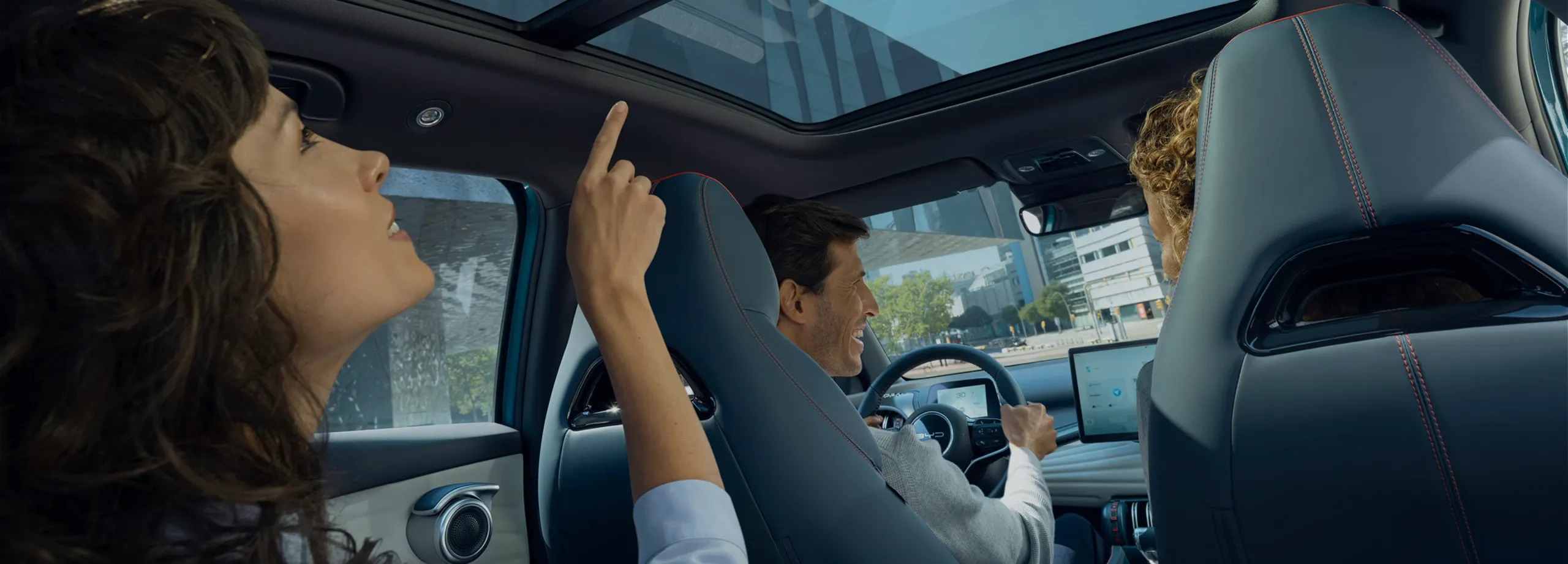 Pessoas com aspeto feliz, no interior de um BYD, onde se vê a pessoa que vai sentada no banco traseiro, a apontar para o teto panorâmico