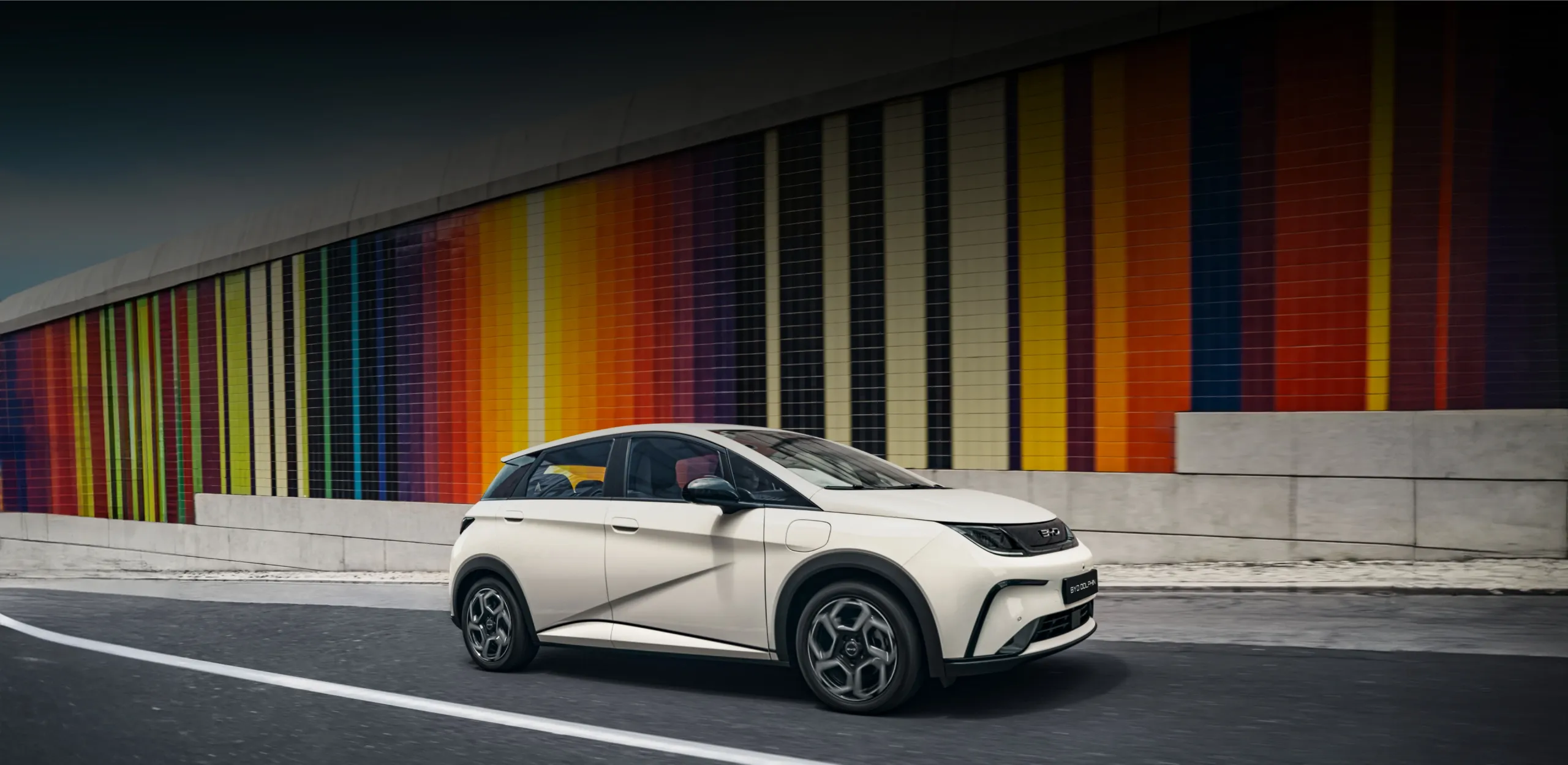 BYD DOLPHIN sobe uma estrada urbana junto a um painel de azulejos coloridos