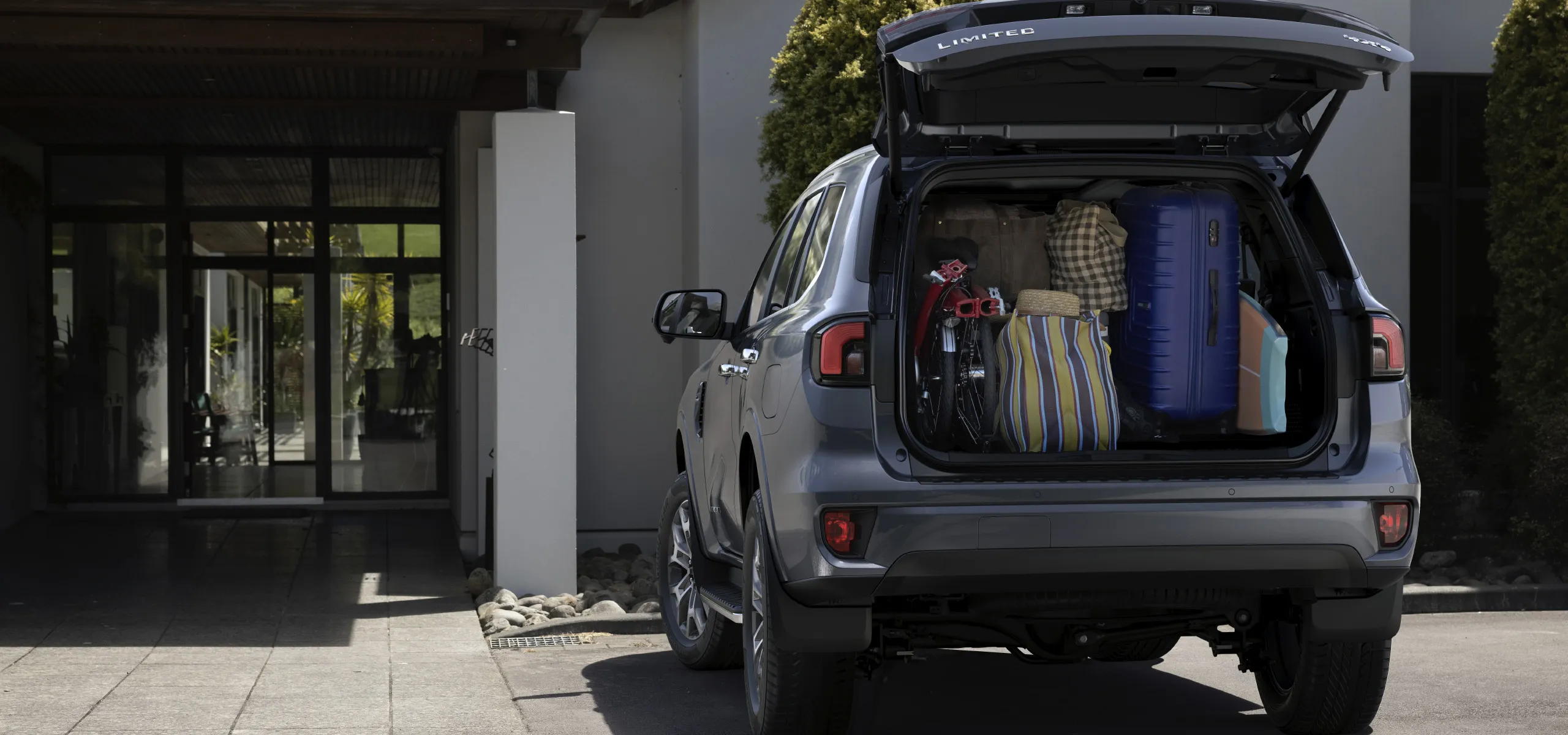 Ford Everest garée devant une maison avec la porte du coffre ouverte et remplie de valises